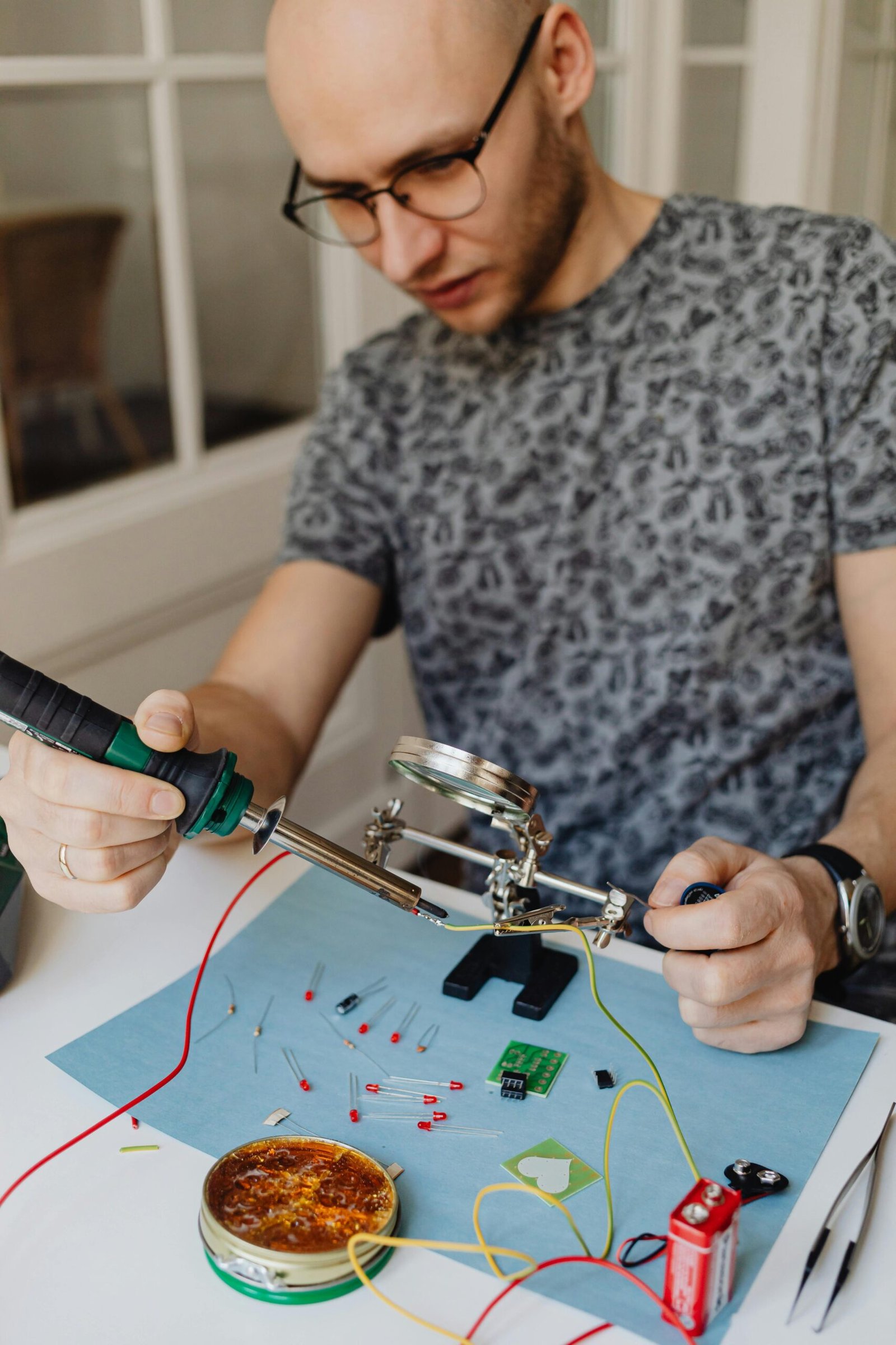 Adult man using soldering iron for electronics repair on work table with tools around.